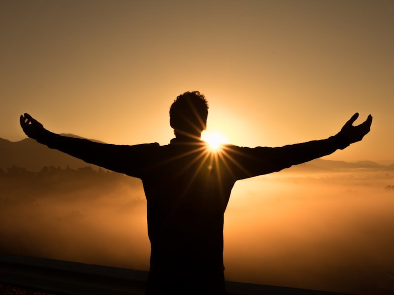 A person standing with arms open toward a sunrise, conveying calm and renewal